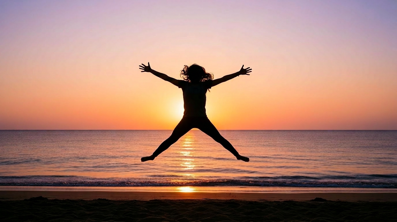 Silhouette of a person joyfully jumping with arms and legs spread wide on a beach at sunset